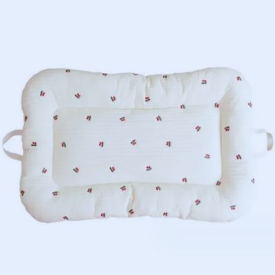Reducteur de lit bebe cocon blanc à motifs cerises, avec poignées latérales, posé sur une surface douce. Design sécurisé et pratique pour le repos des tout-petits.