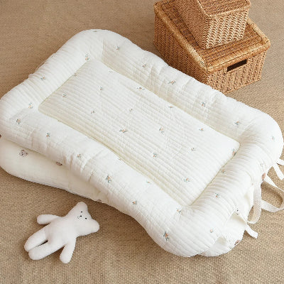 Reducteur de lit bebe cocon blanc matelassĂ© avec motifs discrets, posĂ© sur un tapis texturĂ©, accompagnĂ© dâun doudou et de paniers en osier. Ambiance douce et organisĂ©e, idĂ©ale pour une chambre bĂ©bĂ© chaleureuse.