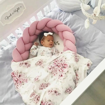 Reducteur de lit bebe : bĂ©bĂ© endormi dans un cocon tressĂ© rose, vĂȘtu dâun ensemble fleuri, couvert dâune couverture florale, sous un mobile doux. Ambiance sereine et sĂ©curisante.