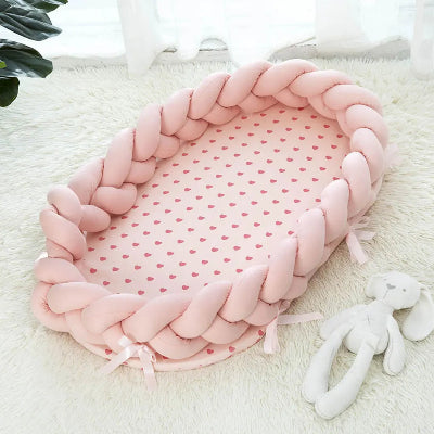 Reducteur de lit bebe : cocon tressĂ© rose posĂ© sur un tapis blanc duveteux, avec matelas Ă cĆurs et doudou lapin. Ambiance douce et sĂ©curisĂ©e.