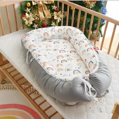 réducteur de lit sur un matelas blanc dans un berceau en bois a cote d'un sapin décoré.