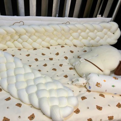 Tour de lit tressé : tresse blanche moelleuse entourant coussin ourson et traversin imprimé, sur drap à motifs oursons dans berceau sécurisé. Confort et douceur pour bébé.