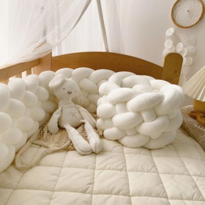 Tour de lit tressé : tresse blanche moelleuse entourant un doudou lapin sur couverture matelassée crÚme, dans un berceau bois clair. Ambiance douce et apaisante.