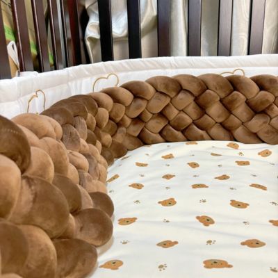 Tour de lit tressé : tresse moelleuse brun dans berceau en bois foncé, sur drap blanc à motifs oursons et fleurs, créant un cocon doux et sécurisé pour bébé.