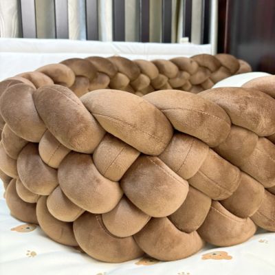 Tour de lit tressé : tresse moelleuse brun dans berceau bois foncé, posée sur drap blanc à motifs pattes et oursons, pour un cocon sécurisé et chaleureux.