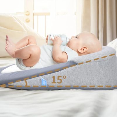 Bébé allongé dans un cocon pour bebe gris à inclinaison 15°, buvant son biberon sur un lit dans une chambre lumineuse et apaisante.