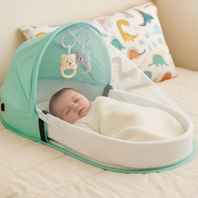 BĂ©bĂ© endormi dans un lit bebe de voyage vert clair avec moustiquaire et jouets suspendus, entourĂ© dâun coussin dĂ©corĂ© de dinosaures dans un cadre paisible.