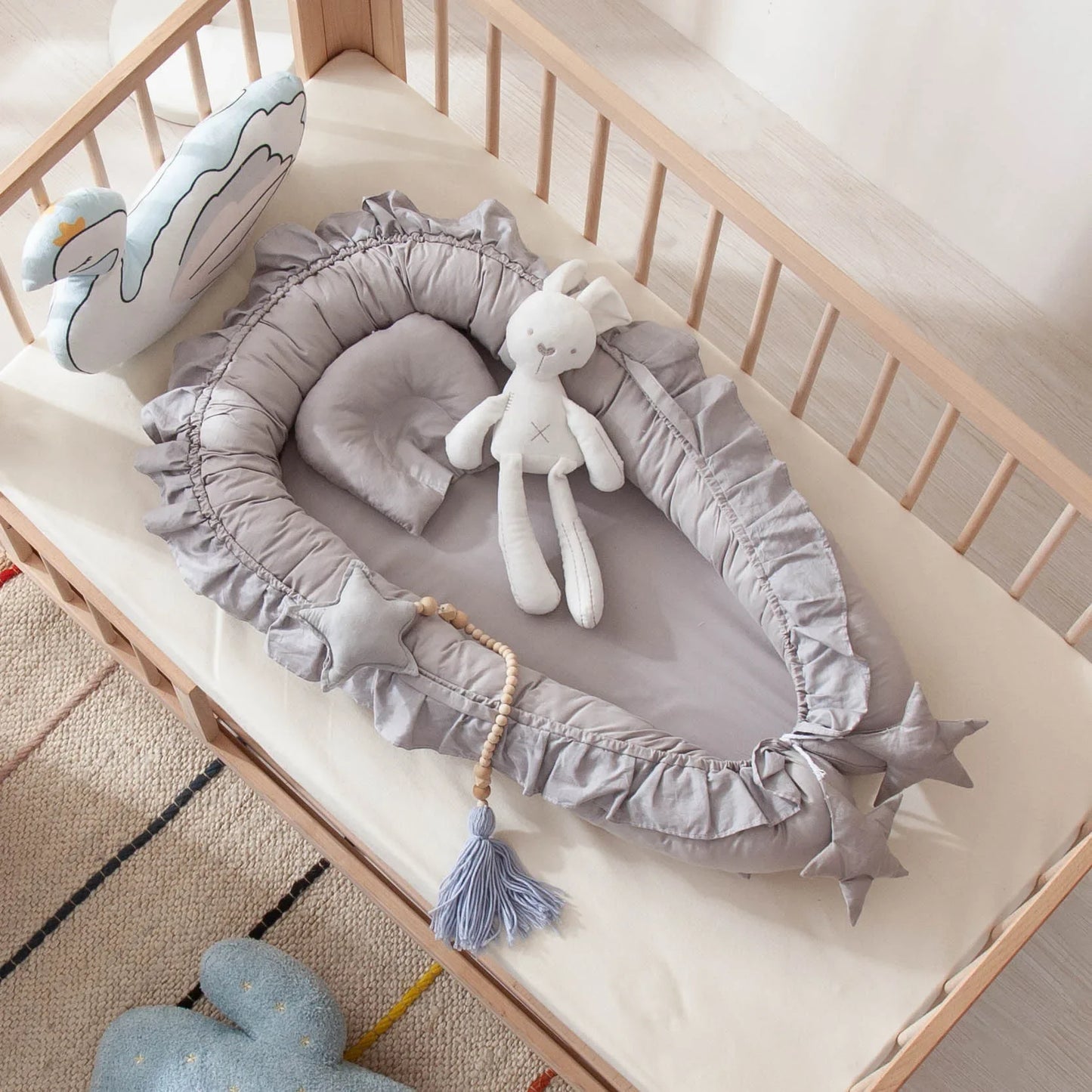 un nid pour bebe couleur gris sur un matelas blanc dans un berceau en bois avec des toutous dans une chambre de bebe
