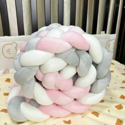 Tour de lit tressé : tresse moelleuse rose, blanche et grise posée sur drap à motifs oursons, dans un berceau aux barreaux foncés. Déco douce et sécurisante.