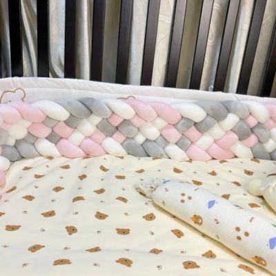 Tour de lit tressé : berceau aux barreaux foncés avec tresse moelleuse rose, blanche et grise, drap à motifs oursons et coussin assorti. Ambiance douce et sécurisante.