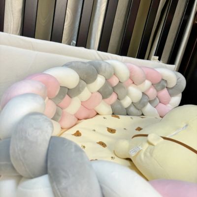 Tour de lit tressé en rose, blanc et gris, installé dans un berceau en bois foncé avec drap à motifs oursons pour une ambiance douce et sécurisée.