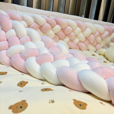 Tour de lit tressé : tresse moelleuse rose et blanche, posée sur drap à motifs oursons et empreintes, dans un décor doux et sécurisé pour bébé.