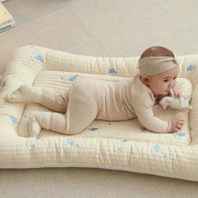 Reducteur de lit bebe : bébé allongé paisiblement sur un matelas matelassé crème à motifs bleus, tenant un doudou rayé. Environnement doux et sécurisé, idéal pour les moments de repos.
