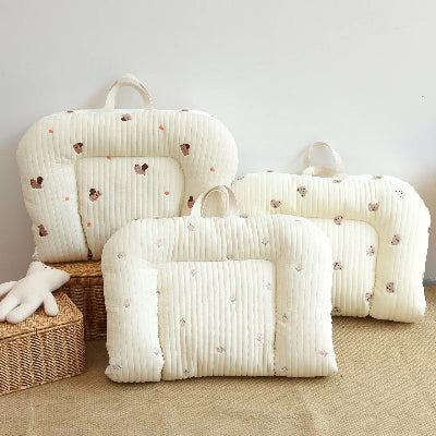 Reducteur de lit bebe trois coussins matelassés crème à motifs cœurs, avec poignées intégrées, posés sur un sol beige près d’un panier en osier et d’un doudou. Ambiance douce et cosy, idéale pour le confort des tout-petits.