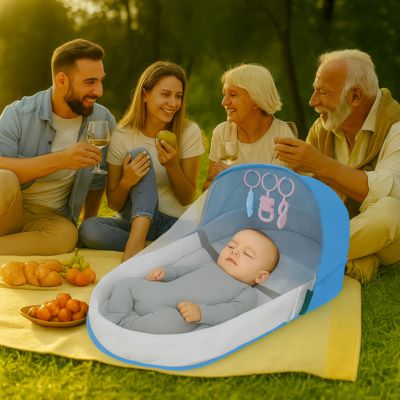 Famille réunie pour un pique-nique dans un parc ensoleillé, avec un bébé dormant paisiblement dans un lit bebe de voyage bleu et blanc, équipé de jouets suspendus. Les parents et grands-parents sont assis sur une couverture jaune, souriants et détendus autour d’un repas convivial.