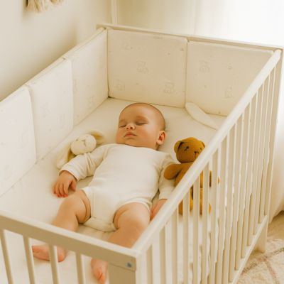 Tour de lit bébé blanc à motifs oursons et étoiles, installé dans un berceau lumineux avec peluches douces pour créer un cocon rassurant et chaleureux à bébé