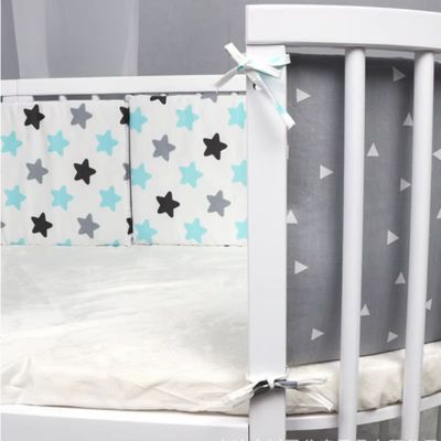 berceau blanc avec tour de lit étoilé bleu, gris et noir, associé à un matelas blanc. Ambiance douce et sécurisée pour bébé.