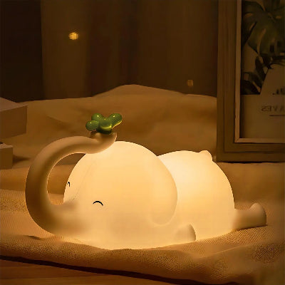 veilleuse éléphant allumé sur une nappe a cote d'un cadre de plante sur une table